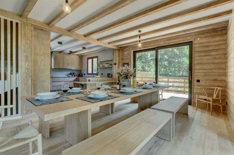 Espace salle à manger donnant sur la cuisine et l'exterieur, grande table en bois avec des bancs sur les cotes le tout dans un esprit chalet familiale